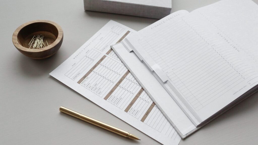A pen and planner on a desk with a notebook.