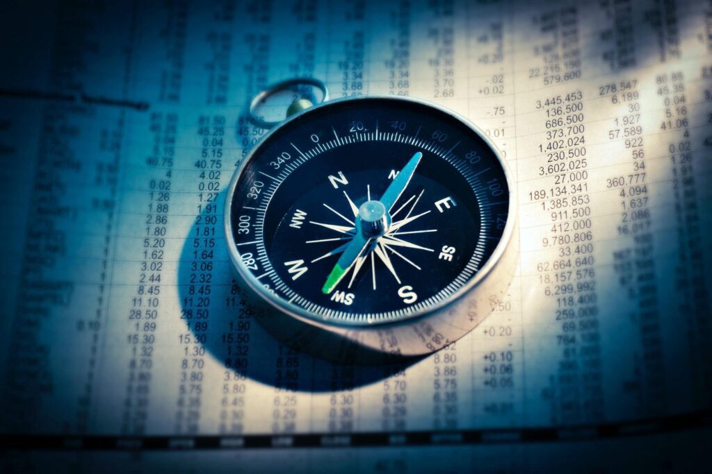 A close-up of a compass on financial data sheets.