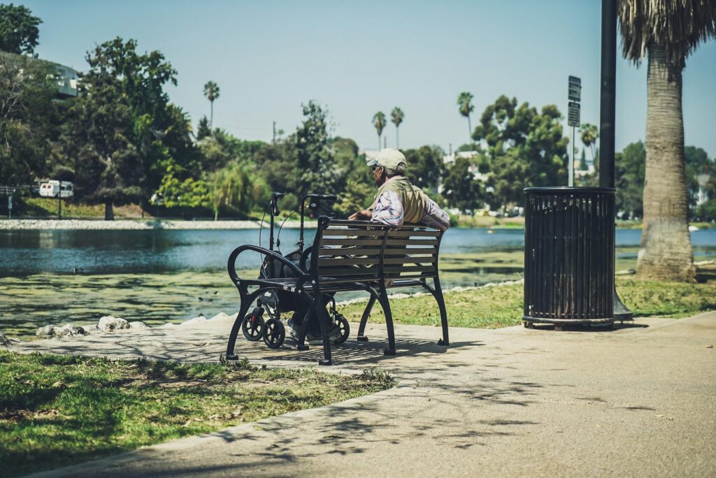 Person sitting alone on a bench by the water under a clear sky.