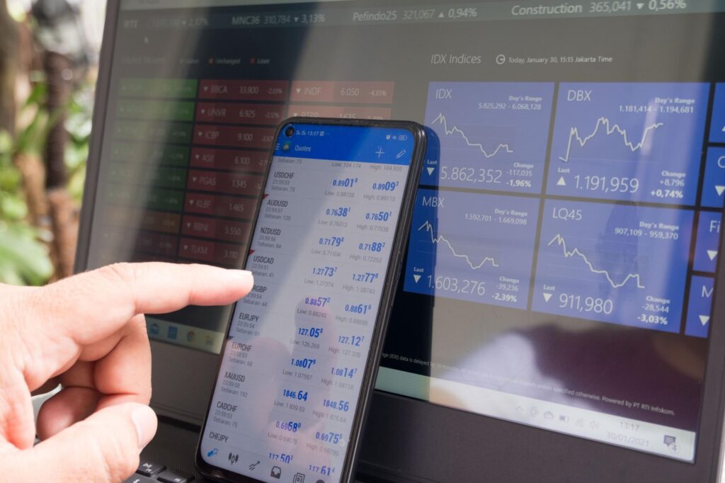 Person checking financial data on smartphone with stock market charts in background.
