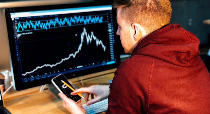 Person analyzing stock market data on smartphone and computer.