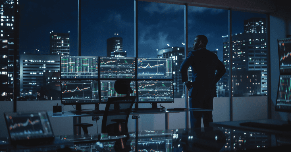 A business professional analyzes financial data on multiple screens in a modern office at night.