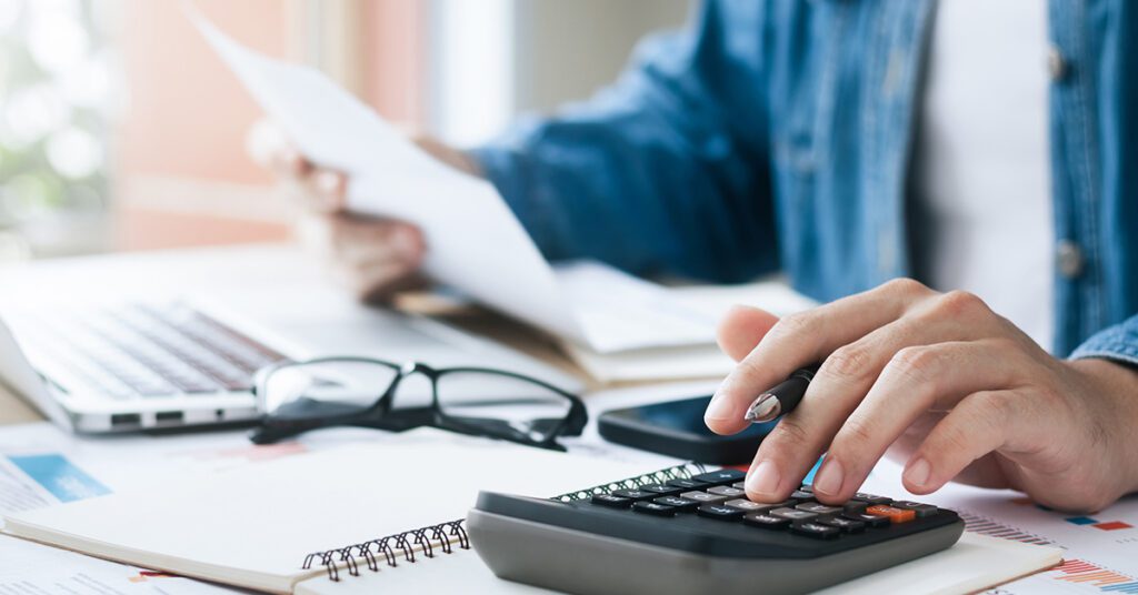Hands using calculator with laptop and documents